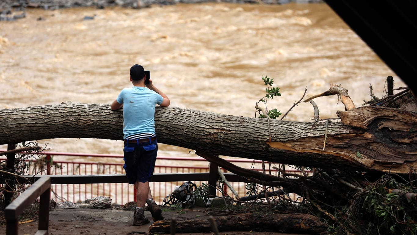Ein Mann lehnt an einem umgekippten Baumstamm und blickt auf das Hochwasser (Archivbild): Im Ahrtal werden erneut schwere Unwetter erwartet.