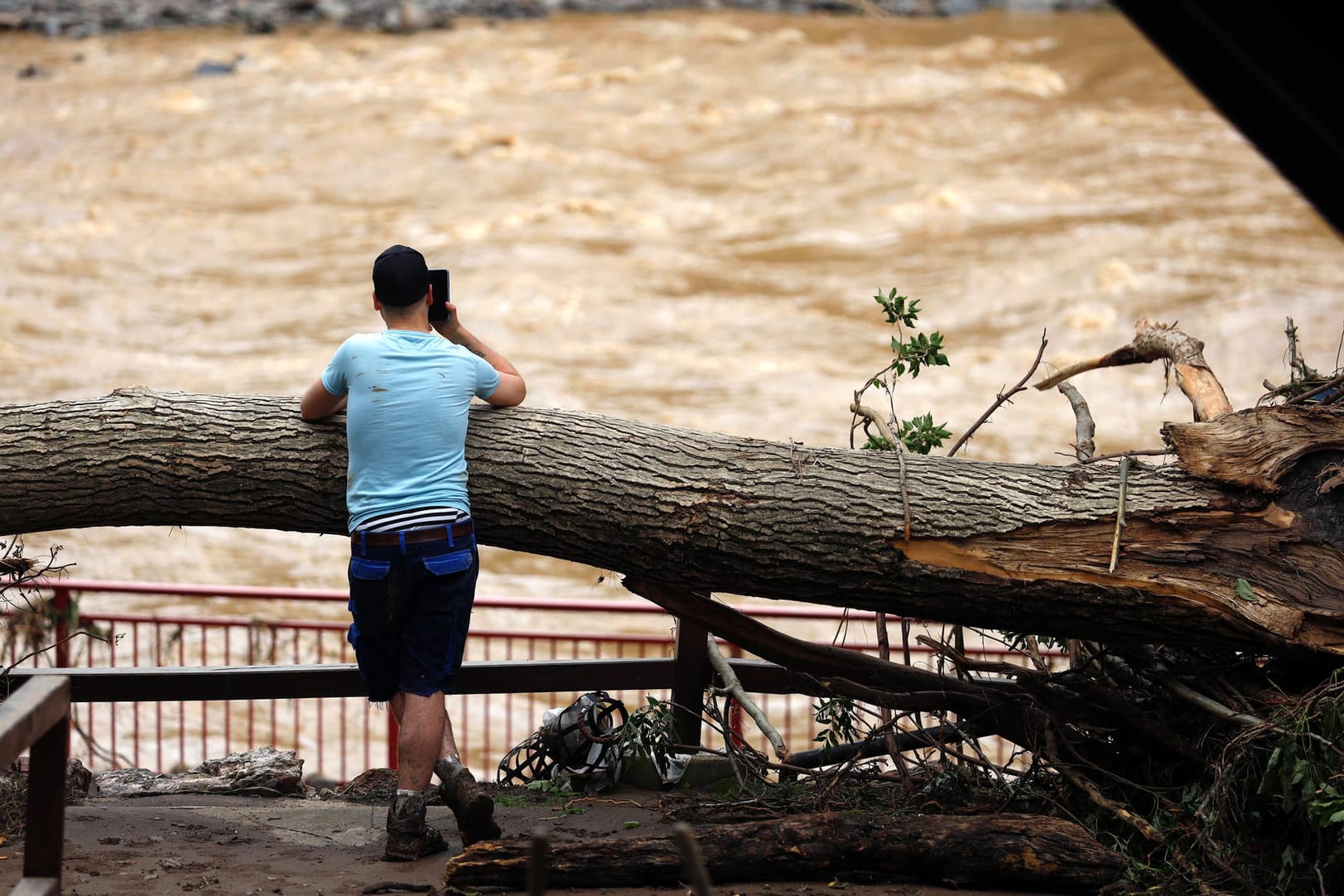 Ein Mann lehnt an einem umgekippten Baumstamm und blickt auf das Hochwasser (Archivbild): Im Ahrtal werden erneut schwere Unwetter erwartet.