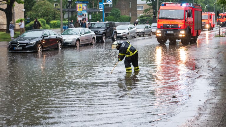 Feuerwehrfrau steht auf einer überfluteten Straße: Auch für Freitag sind in Hamburg Gewitter und Starkregen angesagt.