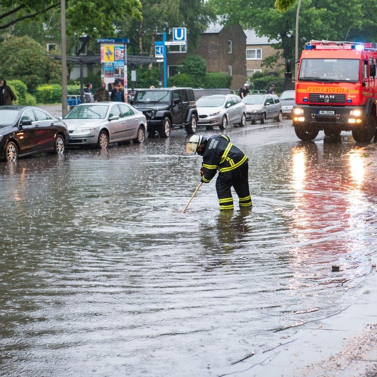 Feuerwehrfrau steht auf einer überfluteten Straße: Auch für Freitag sind in Hamburg Gewitter und Starkregen angesagt.