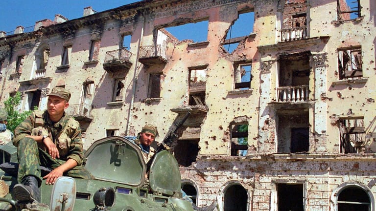 Russische Soldaten patrouillieren im Sommer 2000 auf ihrem Panzer vor einem zerstörten Gebäude in Grosny.