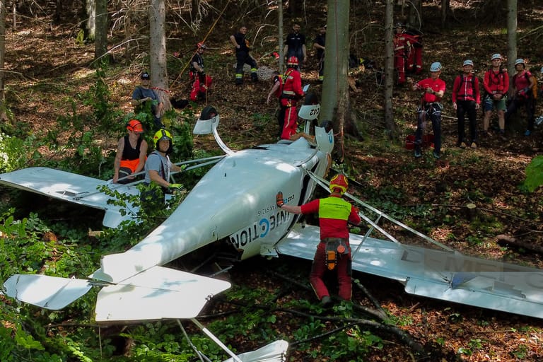 Feuerwehrleute sind neben einem der abgestürzten Flugzeuge im Einsatz. Zwei bayerische Piloten sind bei einem gemeinsamen Flug mit ihren Leichtflugzeugen in Österreich zusammengestoßen.