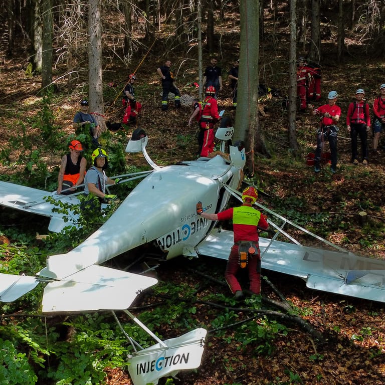Feuerwehrleute sind neben einem der abgestürzten Flugzeuge im Einsatz. Zwei bayerische Piloten sind bei einem gemeinsamen Flug mit ihren Leichtflugzeugen in Österreich zusammengestoßen.