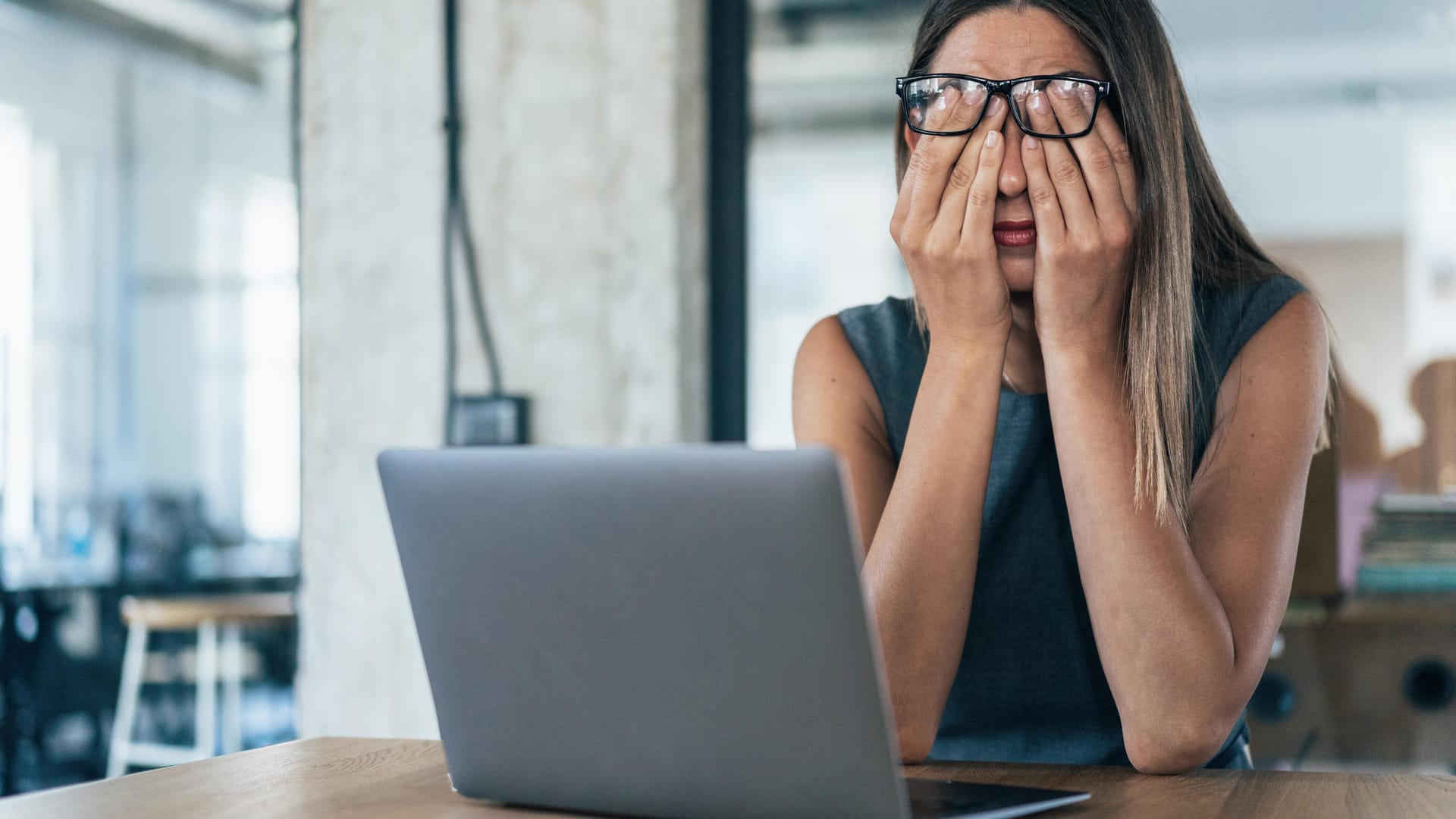 Frau am Laptop bedeckt die Augen mit den Händen.