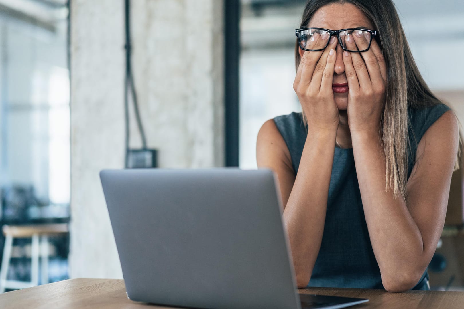 Frau am Laptop bedeckt die Augen mit den Händen.