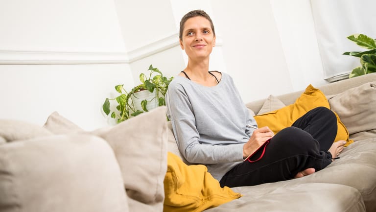 Eine Frau in ihrem Wohnzimmer: Der Heizkostenzuschuss dürfte einigen helfen, die Betriebskostenrechnung entspannter begleichen zu können.