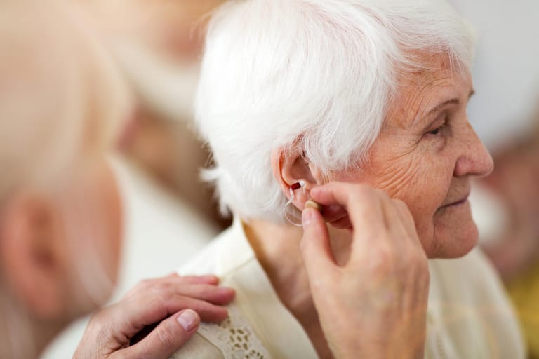 Ärztin setzt Seniorin ein Hörgerät ein: Altersschwerhörigkeit: Im Alter nimmt die Hörleistung ab. Der Prozess beginnt etwa ab dem 50. Lebensjahr. Altersschwerhörigkeit entsteht dadurch, dass die winzig kleinen Haarzellen in der Hörschnecke (Cochlea) nicht mehr vorhanden sind oder beschädigt werden. Ein Hörgerät kann helfen, das Hörvermögen zu optimieren.