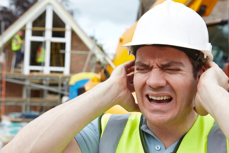 Bauarbeiter hält sich die Ohren zu: Akute und chronische Schäden durch Lärm: Starker Lärm etwa durch Explosionen, Knall oder sehr laute Musik können Hörstörungen verursachen. Der Schweregrad eines akuten Traumas ist anhängig von der Lautstärke und der Einwirkungszeit. Bei dauerhafter Belastung des Ohres kann eine anhaltende Schwerhörigkeit die Folge sein.