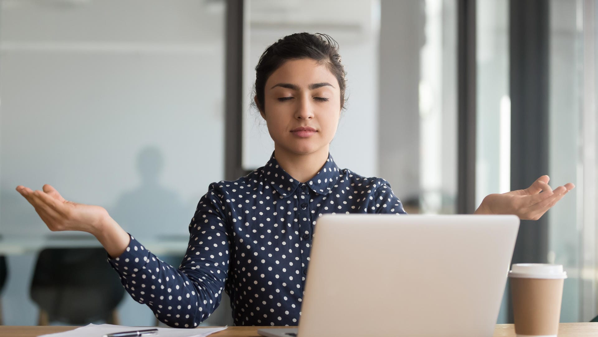 Junge Frau meditiert im Büro: Bürojobs können ziemlich stressig sein. Kurze Meditationseinheiten können helfen, den Kopf wieder frei zu bekommen.