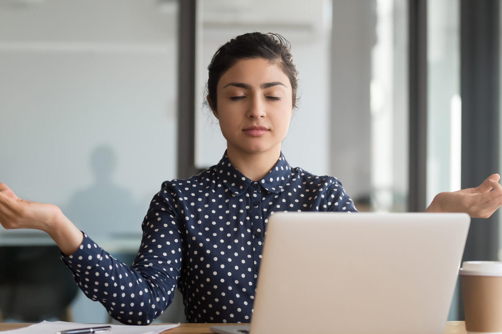 Junge Frau meditiert im Büro: Bürojobs können ziemlich stressig sein. Kurze Meditationseinheiten können helfen, den Kopf wieder frei zu bekommen.