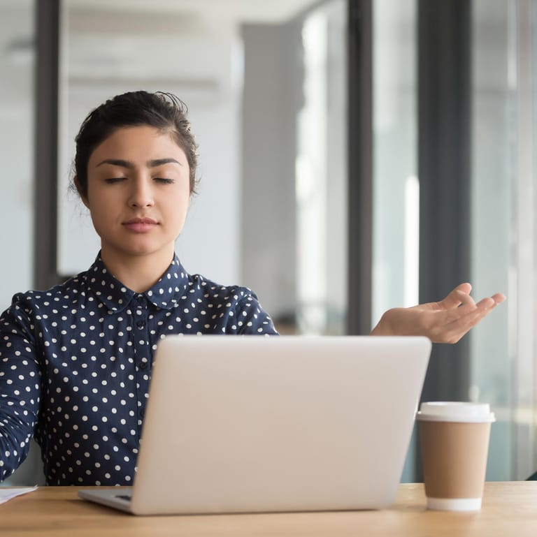 Junge Frau meditiert im Büro: Bürojobs können ziemlich stressig sein. Kurze Meditationseinheiten können helfen, den Kopf wieder frei zu bekommen.