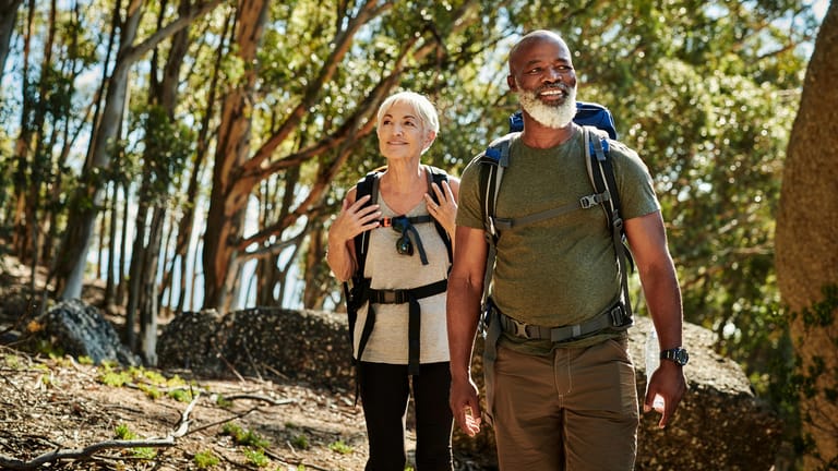 Ältere Frau und Mann bei Wandern im Wald: Viel Bewegung ist wichtig für den Erhalt der Muskeln und einen gesunden Körper. Wandern ist eine gute Möglichkeit, fit zu bleiben und kann zusätzlich beruhigend wirken.