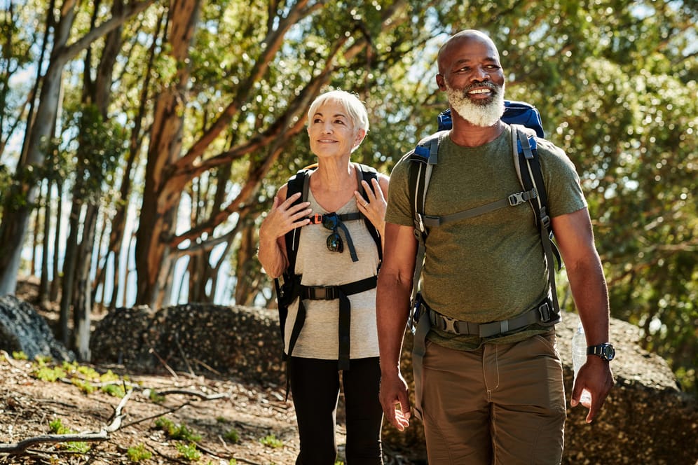 Ältere Frau und Mann bei Wandern im Wald: Viel Bewegung ist wichtig für den Erhalt der Muskeln und einen gesunden Körper. Wandern ist eine gute Möglichkeit, fit zu bleiben und kann zusätzlich beruhigend wirken.