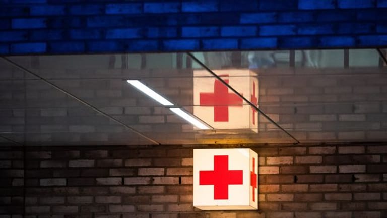 Ein rotes Kreuz vor einer Notaufnahme (Symbolbild): Nach dem Stromunfall im Münchner Bahnhof Trudering sind zwei Verletzte im künstlichen Koma.