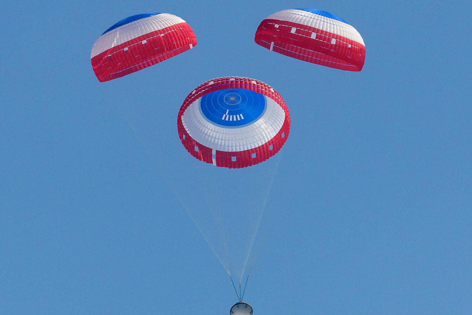 Ein Bild der Nasa zeigt die Starliner-Kapsel an Fallschirmen hängend.