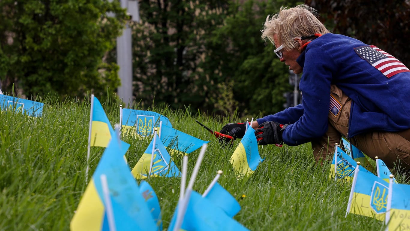 Ein Mann pflegt eine Gedenkstätte in Kiew (Archiv): Blau-gelbe Fähnchen tragen die Nahmen von Opfern des russischen Angriffskriegs.