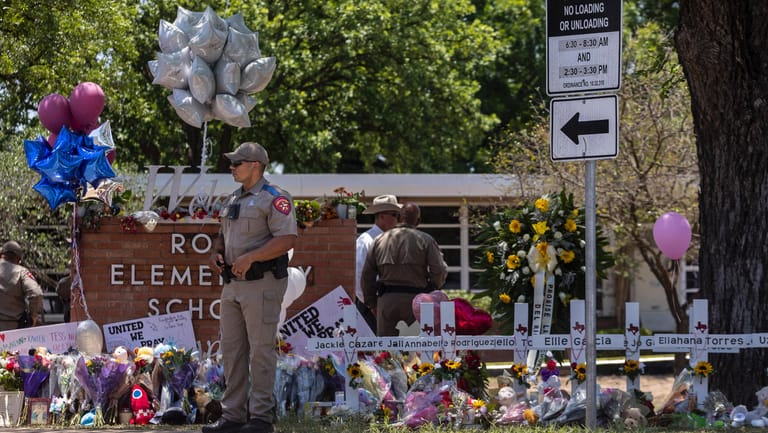 Polizisten stehen vor niedergelegten Blumen und Kreuzen, die an die Opfer des Amoklaufs von Uvalde erinnern.