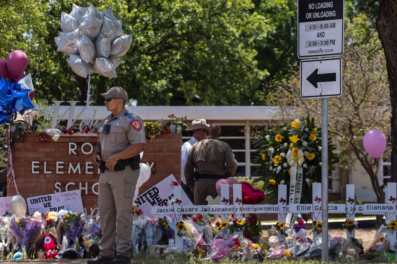 Polizisten stehen vor niedergelegten Blumen und Kreuzen, die an die Opfer des Amoklaufs von Uvalde erinnern.