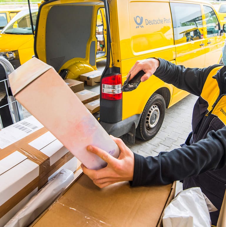DHL-Mitarbeiter scannt Pakete (Symbolbild): Viele Händler verlangen bisher keine Rücksendegebühren. Entsprechend viel Arbeit haben Lieferdienste mit Retouren.ete mit einem