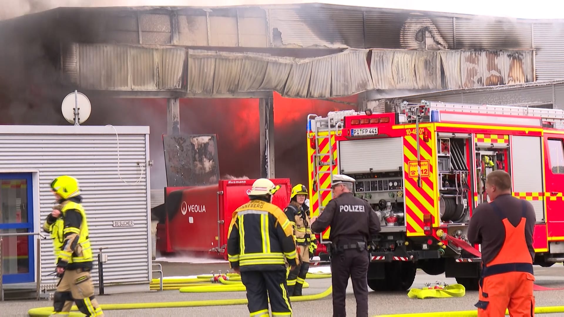 Einsatzkräfte von Polizei und Feuerwehr stehen vor der brennenden Lagerhalle. Einsatzkräfte von Polizei und Feuerwehr stehen vor der brennenden Lagerhalle.