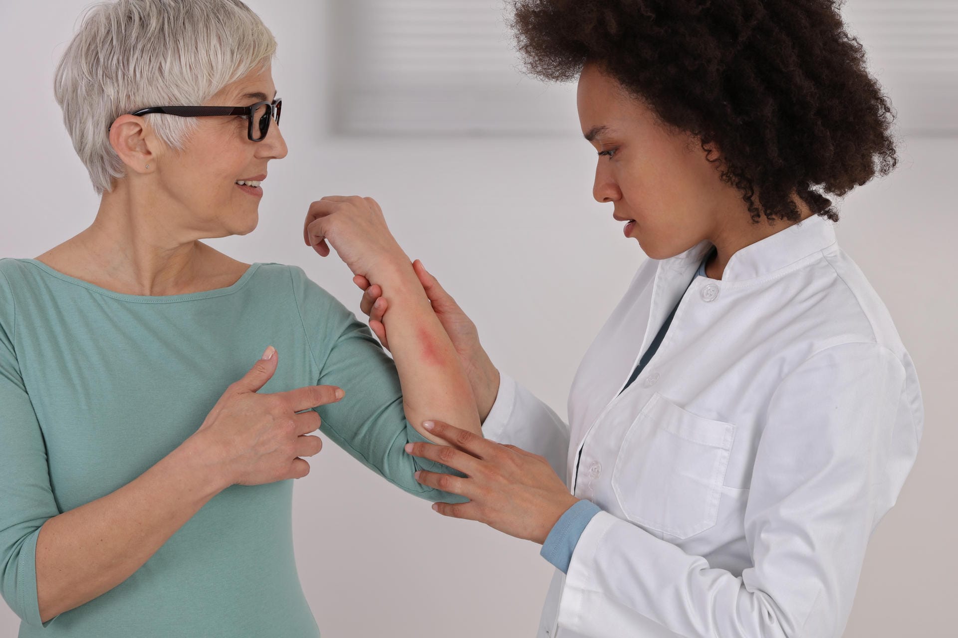 Eine Frau zeigt einer Ärztin eine Hautstelle am Unterarm.
