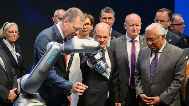 Bundeskanzler Olaf Scholz (M, SPD) und Antonio Costa (r), Premierminister von Portugal, betrachten neben Oliver Jung, Vorstandsvorsitzender Festo beim Eröffnungsrundgang auf der Hannover Messe 2022 einen Roboter mit pneumatischem Antrieb.