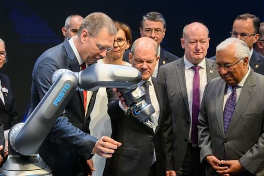 Bundeskanzler Olaf Scholz (M, SPD) und Antonio Costa (r), Premierminister von Portugal, betrachten neben Oliver Jung, Vorstandsvorsitzender Festo beim Eröffnungsrundgang auf der Hannover Messe 2022 einen Roboter mit pneumatischem Antrieb.