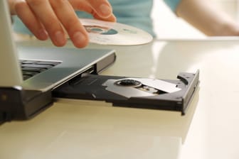 Junge Frau legt eine CD in das Laufwerk am Laptop ein.