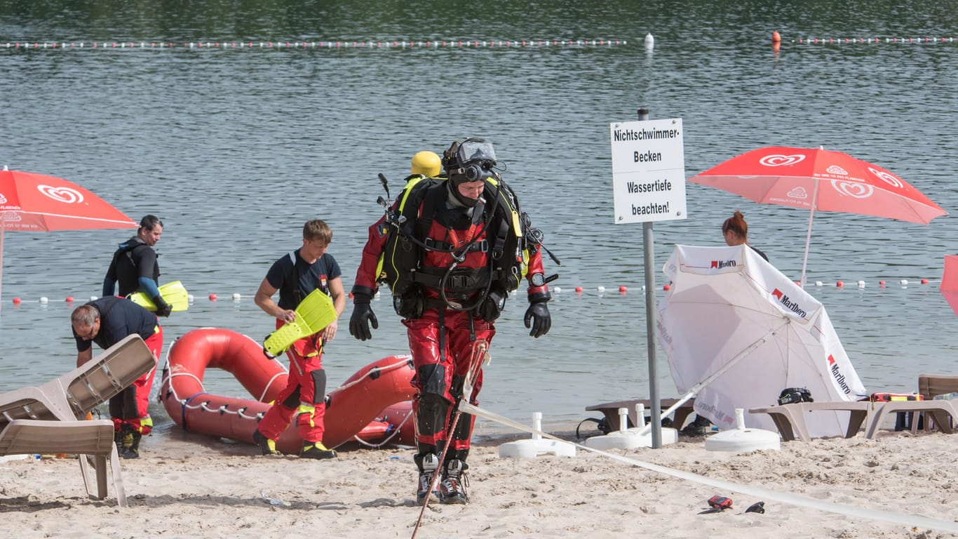 Ein Rettungstaucher geht über den Strand eines Badesees: In Hürth bei Köln ist ein 18-Jähriger infolge eines Badeunfalls verstorben.