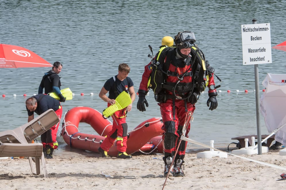 Ein Rettungstaucher geht über den Strand eines Badesees: In Hürth bei Köln ist ein 18-Jähriger infolge eines Badeunfalls verstorben.