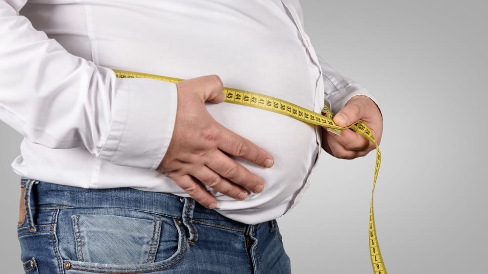 Ein übergewichtiger Mann misst seinen Bauchumfang: Adipositas erhöht das Risiko für viele Krankheiten.