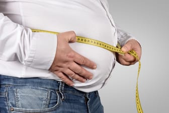 Ein übergewichtiger Mann misst seinen Bauchumfang: Adipositas erhöht das Risiko für viele Krankheiten.