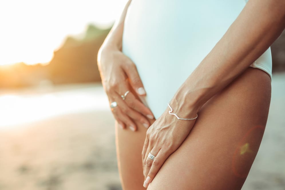 Eine Frau im Badeanzug am Strand: In den Sommermonaten ist Intimhygiene besonders wichtig, da Keime die Kombination von Feuchtigkeit und Wärme besonders "mögen".