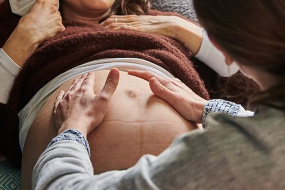 Eine Hebamme tastet den Bauch einer Schwangeren ab.