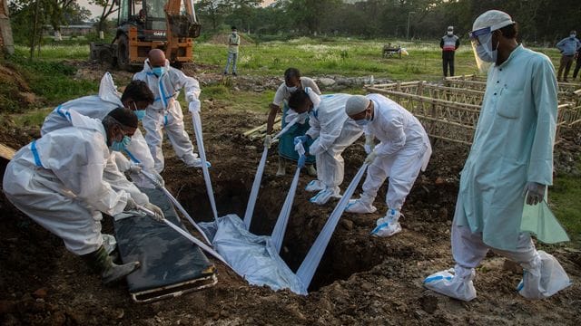 Angehörige und städtische Mitarbeiter in Schutzanzügen begraben in Indien den Körper einer Person, die an Covid-19 gestorben ist.