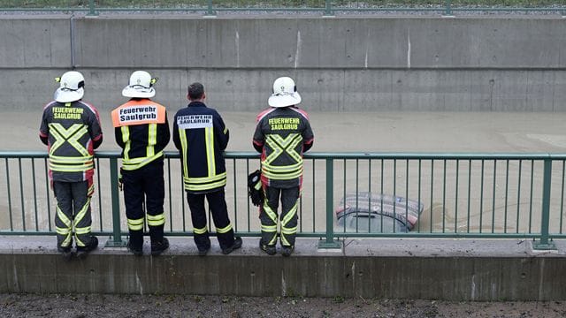 Einsatzkräfte der Feuerwehr schauen auf die Heckklappe eines Autos, das aus dem Wasser auf der teilweise überfluteten Bundesstraße B23 ragt. Einsatzkräfte der Feuerwehr schauen auf die Heckklappe eines Autos, das aus dem Wasser auf der teilweise überfluteten Bundesstraße B23 ragt.