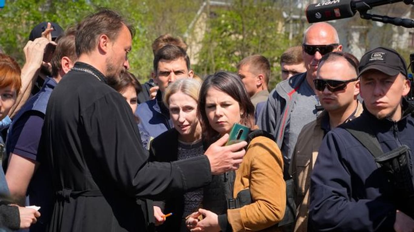 In der Nähe eines Massengrabes in Butscha spricht Annalena Baerbock mit einem örtlichen Priester, der der Außenministerin Bilder auf seinem Smartphone zeigt.