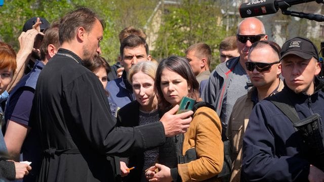 In der Nähe eines Massengrabes in Butscha spricht Annalena Baerbock mit einem örtlichen Priester, der der Außenministerin Bilder auf seinem Smartphone zeigt.