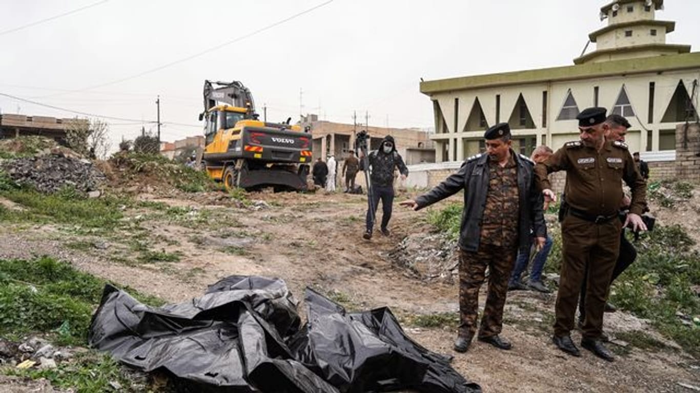 Mitglieder der Sicherheitskräfte zeigen auf einen Leichensack mit menschlichen Überresten, der in einem Massengrab im Westen von Mossul entdeckt wurde.