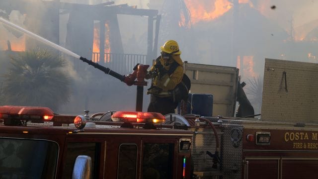Ein Feuerwehrmann vom Costa Mesa Fire Department löscht in Laguna Niguel ein Haus, das während eines Lauffeuers in Brand geraten ist.