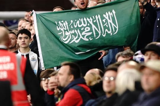 Ein Fan von Newcastle United hält die Fahne von Saudi-Arabien während eines Spiels hoch.