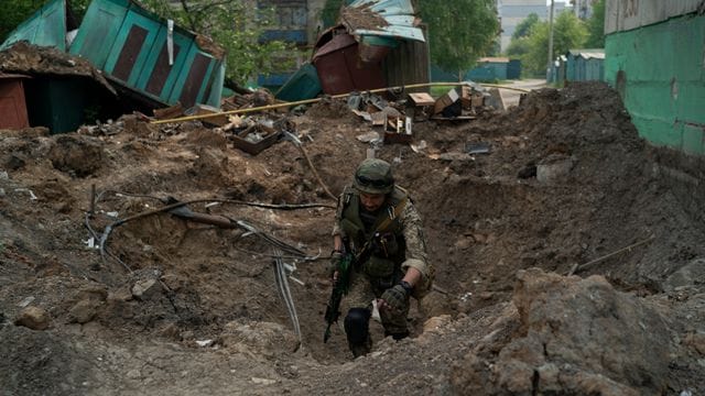 Ein Uniformierter inspiziert einen Krater nach einem Luftangriff der russischen Streitkräfte in der Region Luhansk.