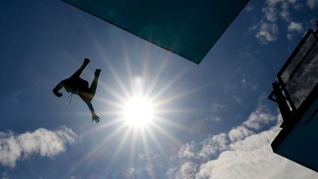 Ein Mann springt im Freibad vom Zehn-Meter-Turm.