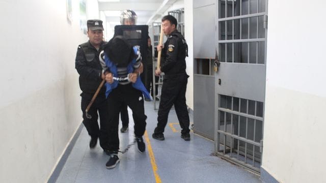 Das Foto aus den Xinjiang Police Files soll Polizisten im Jahr 2018 in einem Umerziehungslager bei einer Festnahme zeigen. Das Foto aus den Xinjiang Police Files soll Polizisten im Jahr 2018 in einem Umerziehungslager bei einer Festnahme zeigen.