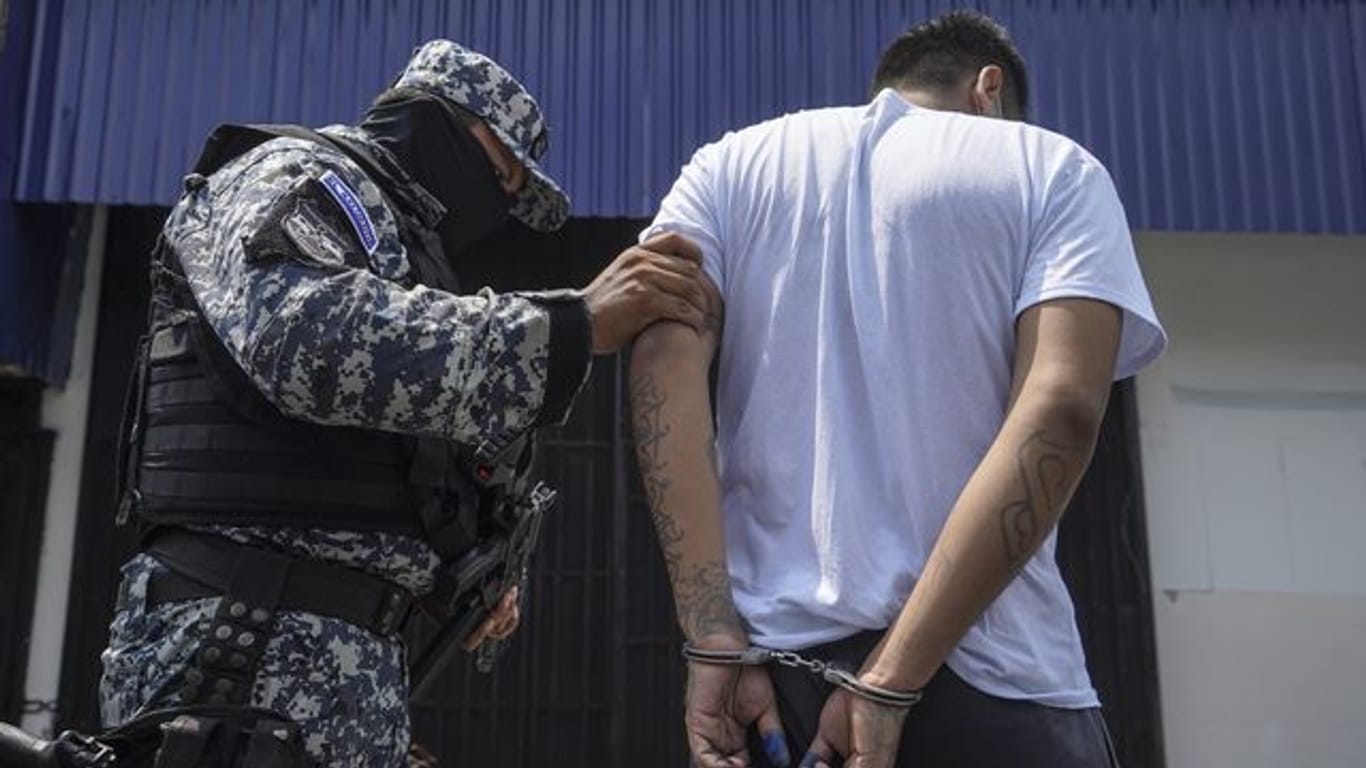 Ein vermummter Polizist in begleitet einen mutmaßlichen Mitglied einer Bande nach dessen Festnahme in San Salvador.