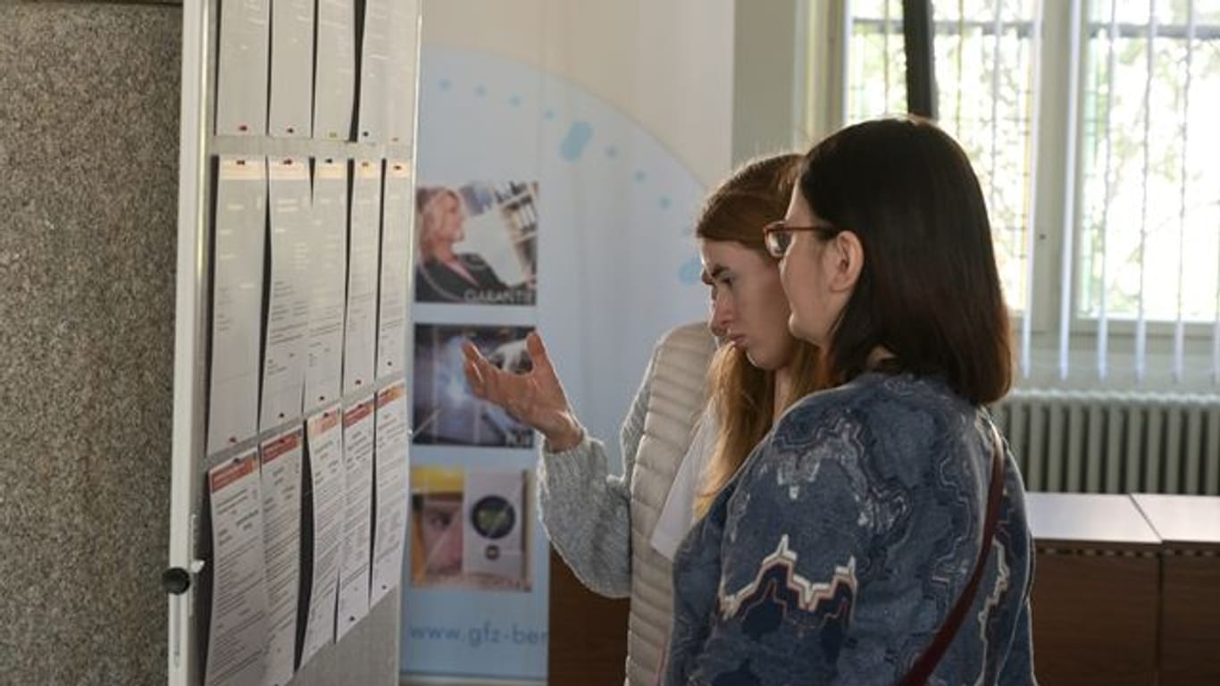 Frauen, die aus der Ukraine geflüchtet sind, informieren sich an einer Tafel über Arbeitsangebote.