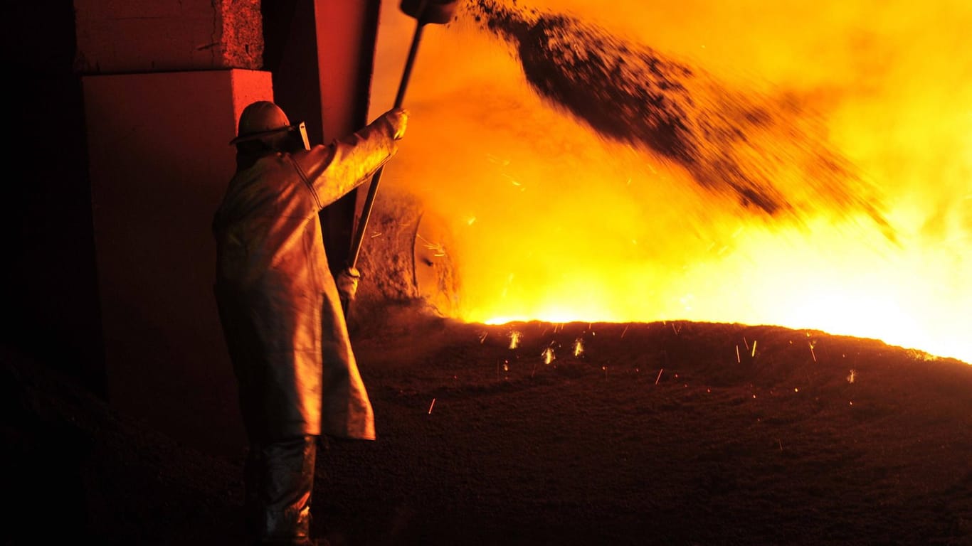 Ein Stahlarbeiter streut Kalk in das heiße Roheisen, das aus einem Hochofen abgelassen wird.