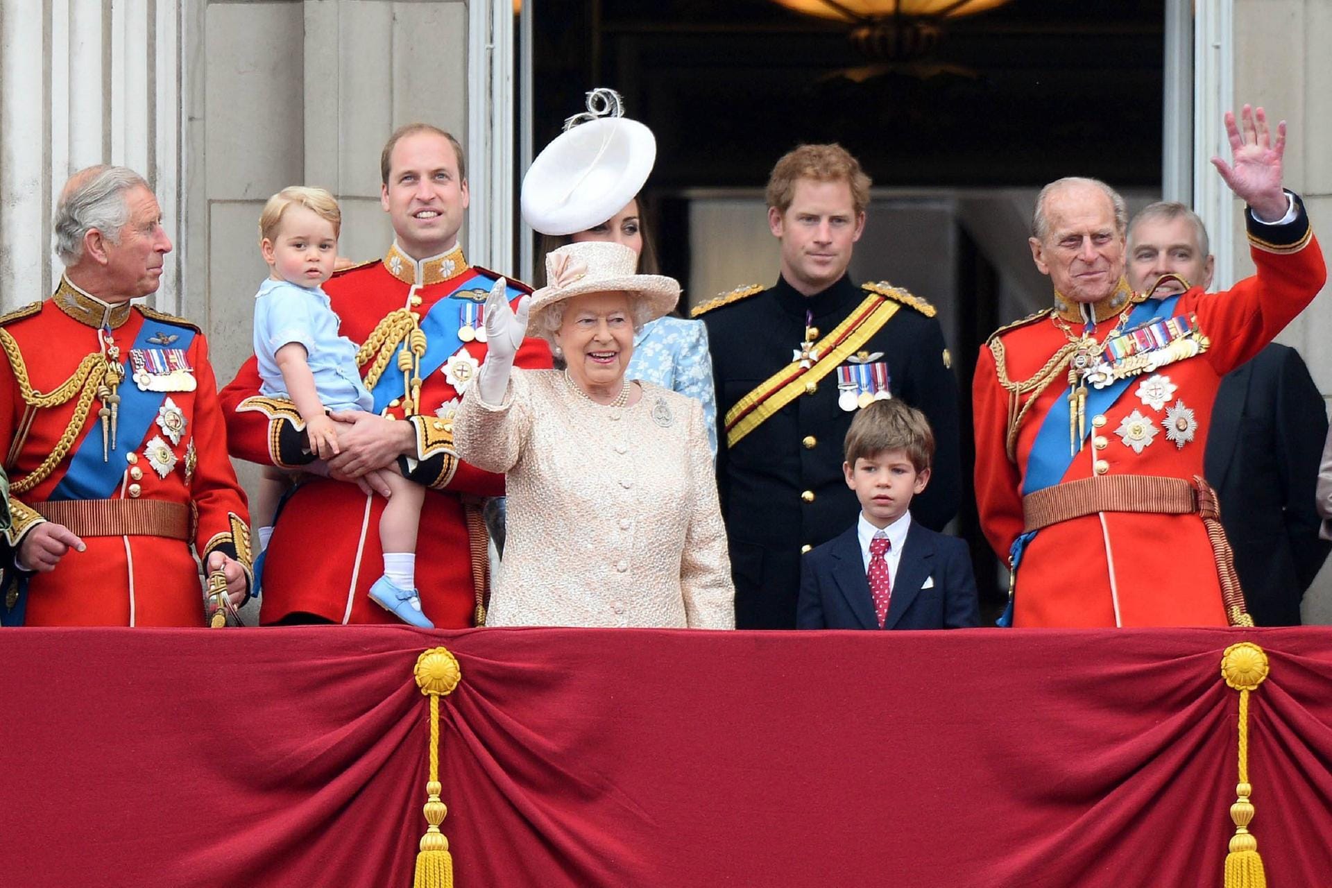 2015: Die Queen winkt strahlend ins Publikum. Links von ihr stehen ihr Sohn Prinz Charles und ihr Enkel Prinz William, der seinen Sohn Prinz George auf dem Arm hält. Hinter ihr steht Herzogin Kate. Rechts von der Monarchin sieht man ihren Enkel Prinz Harry, Prinz James Mountbatten-Windsor, ihren Mann Prinz Philip und ihren Sohn Prinz Andrew.