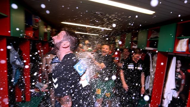 Der Magdeburger Trainer Bennet Wiegert wird in der Mannschaftskabine mit Sekt bespritzt.