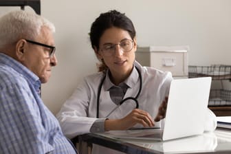 Eine Ärztin zeigt einem Patienten etwas auf einem Laptop.